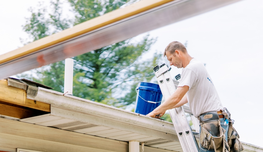 Valley Roofing team member on a ladder and cleaning out gutters.